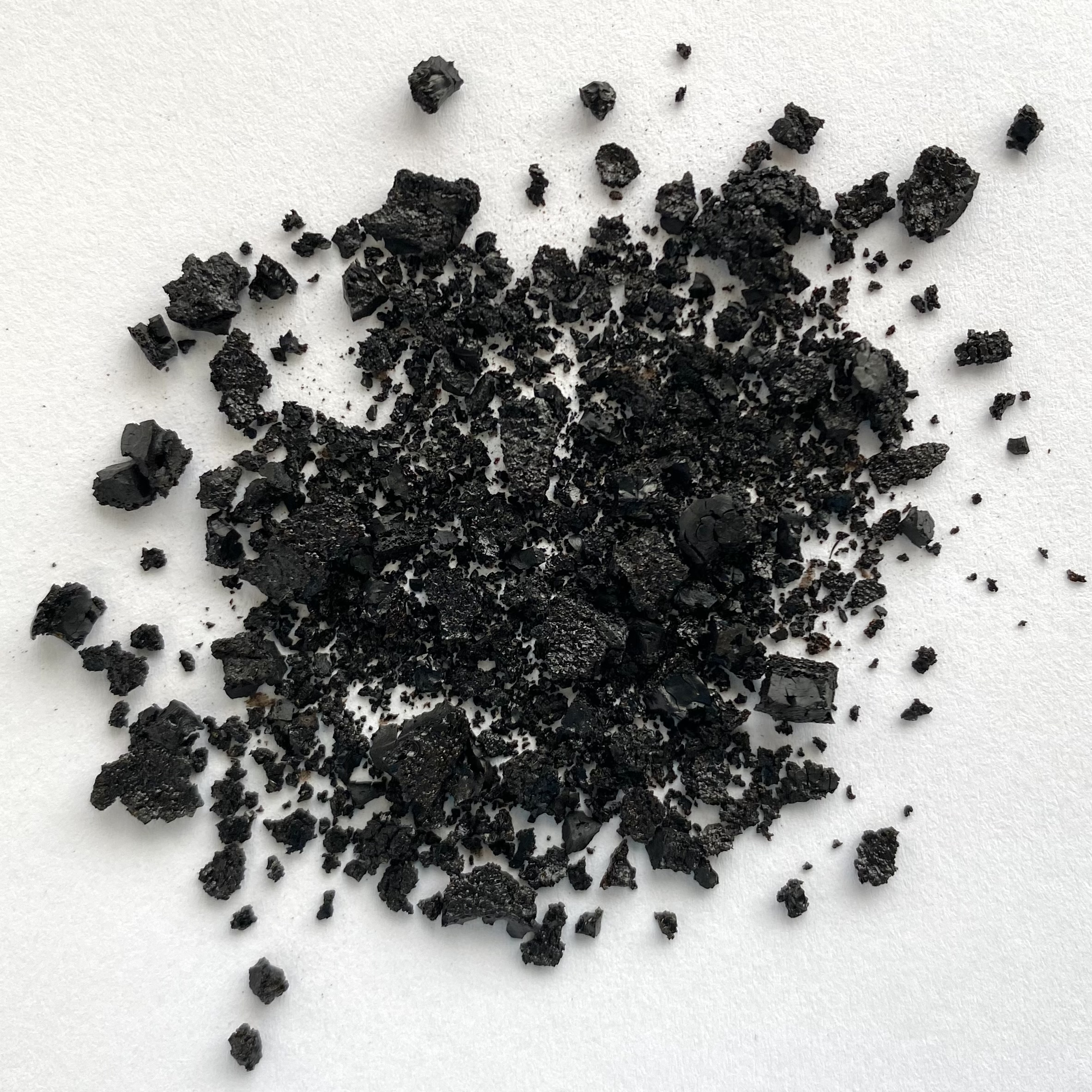 Schwarze Huminsäure-Kristalle und -Fragmente auf hellem Untergrund